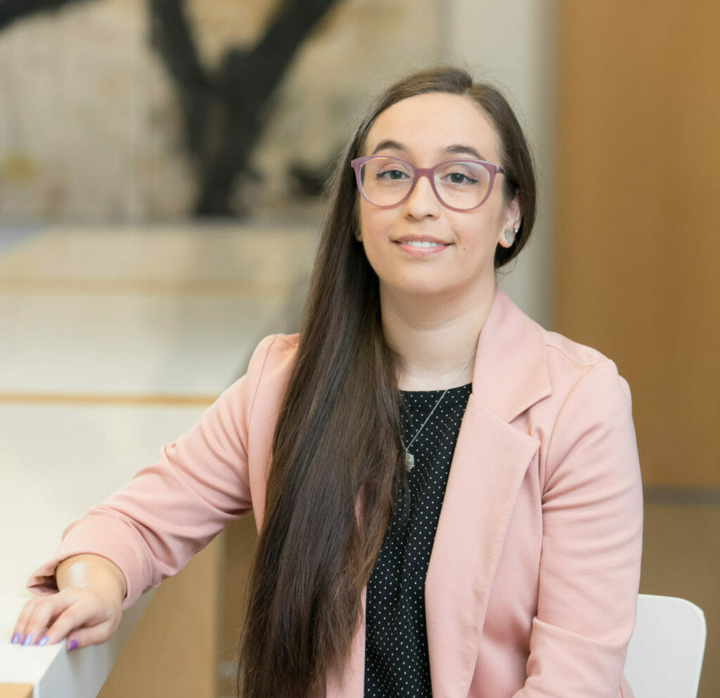 Woman with glasses in a pink blazer and black shirt sitting and smiling